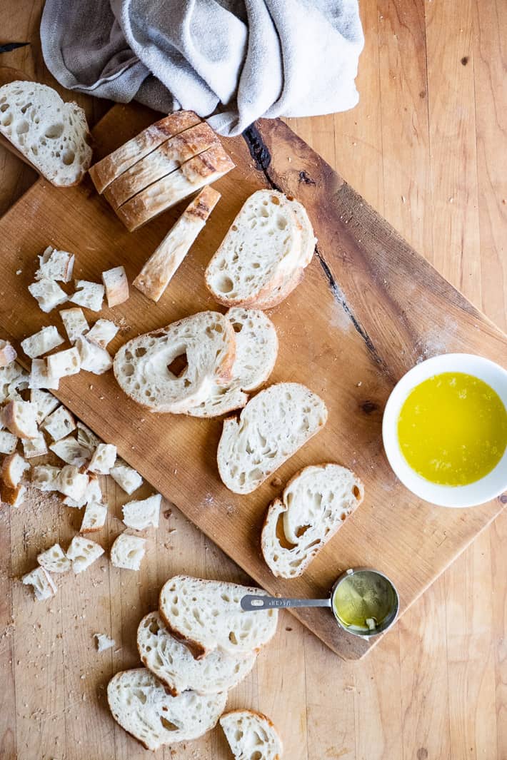 Overhead look at crusty loaves sliced and cubed for homemade croutons with a bowl of melted butter to the side.