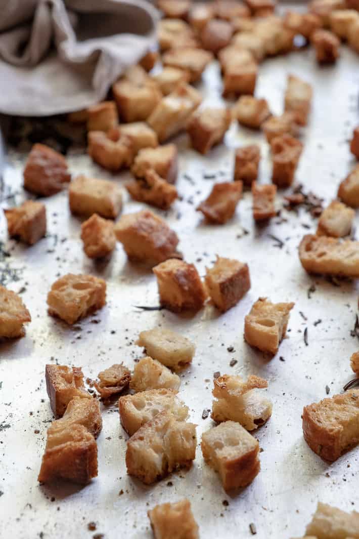 A close up view of browned, airy croutons on a baking sheet with a linen tea towel to the side.