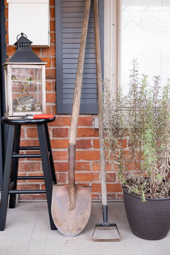 Rusty shovel with broken handle prior to replacing the handle, propped against brick wall of house.