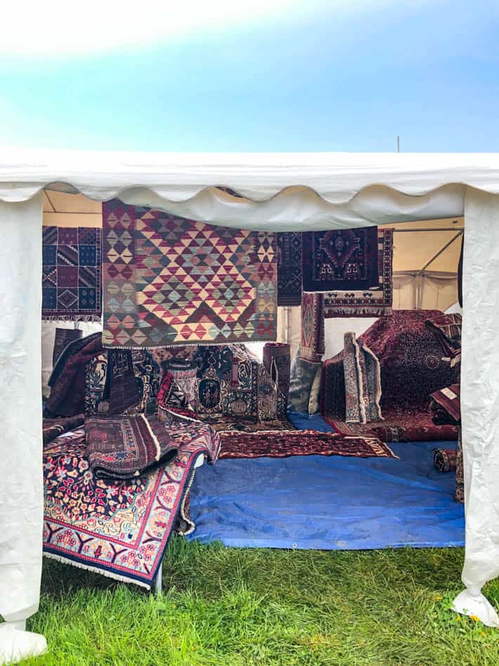 White tent containing many kilim rugs on ground and hanging up at the Christie Antique Show. 