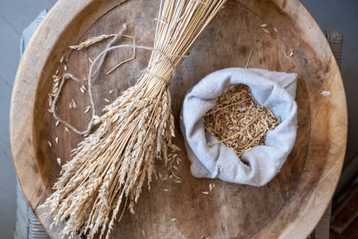 A small sheaf of wheat laid on a round wood platter with a linen bag filled with newly threshed wheat berries.