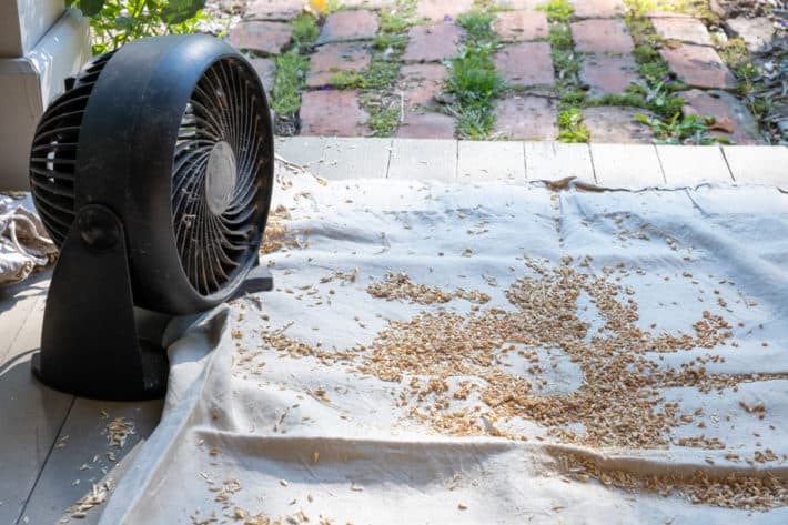 A small cheap fan on a porch directed at wheat with chaff to help with winnowing.