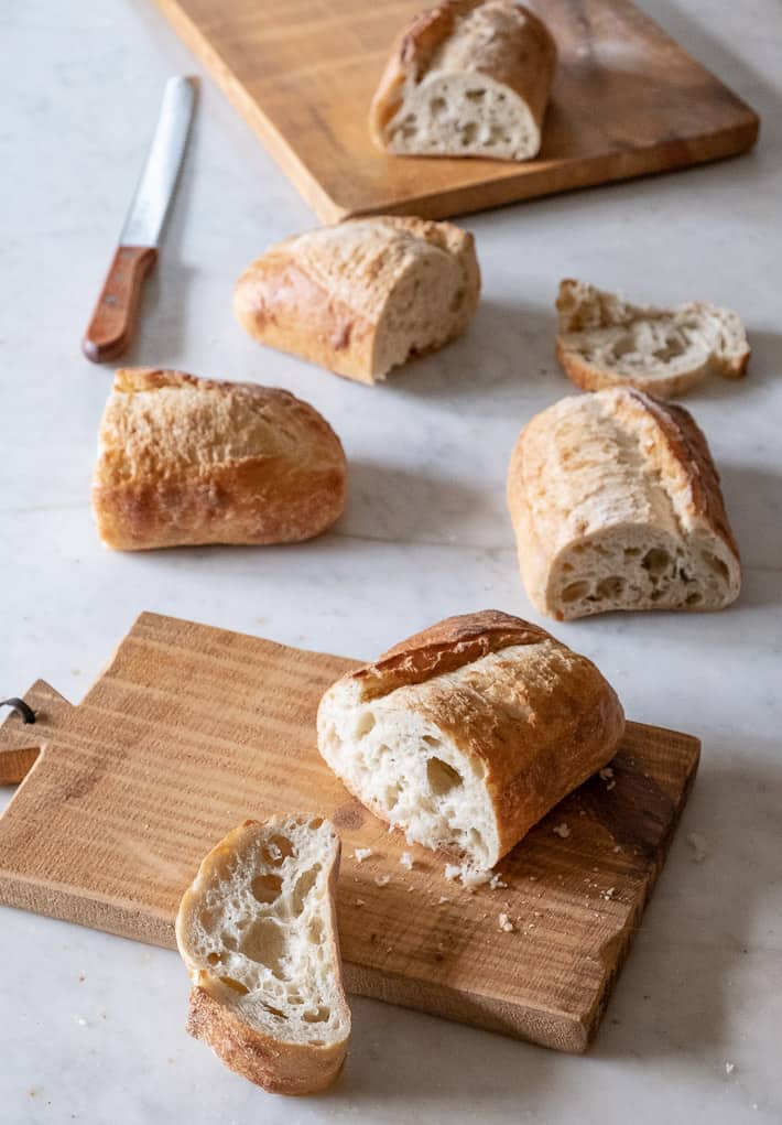 Several fresh loaves of bread cut in half on wood cutting boards.