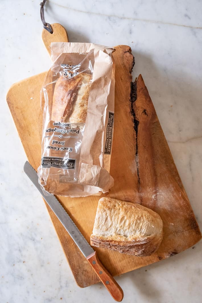 Paper and plastic bag used to bring fresh bread home from the bakery on a wood cutting board.