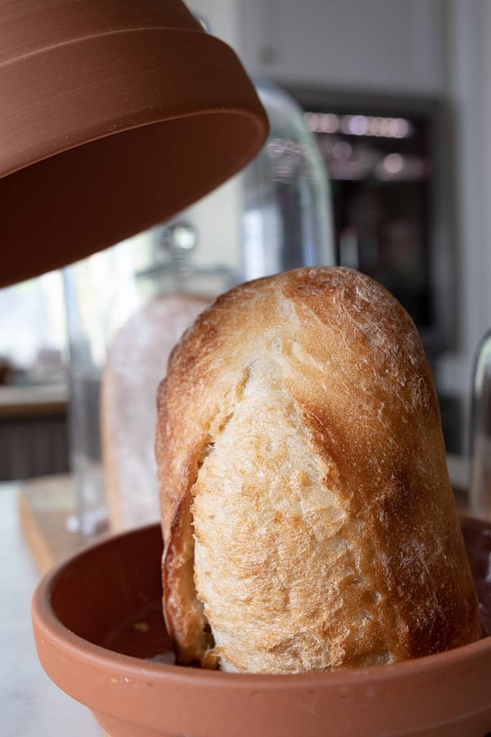 Want fresh bread? Try one of these methods. Pulling the clay lid off of a pot, storing bread.