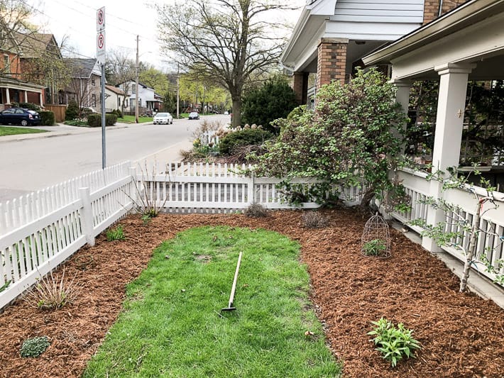 Newly mulched garden beds with a small area of grass, confined within a white picket fence.