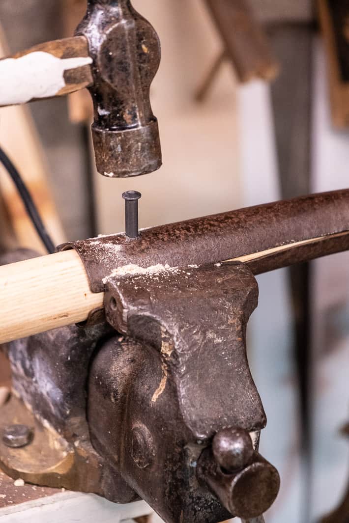 Hammer aimed over new rivet being placed through hole while replacing old shovel handle with new.