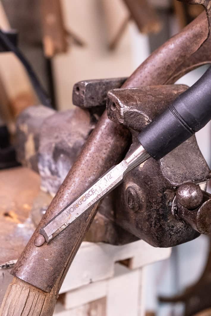 Chisel sliding under head of rivet head on shovel handle being held in vice.