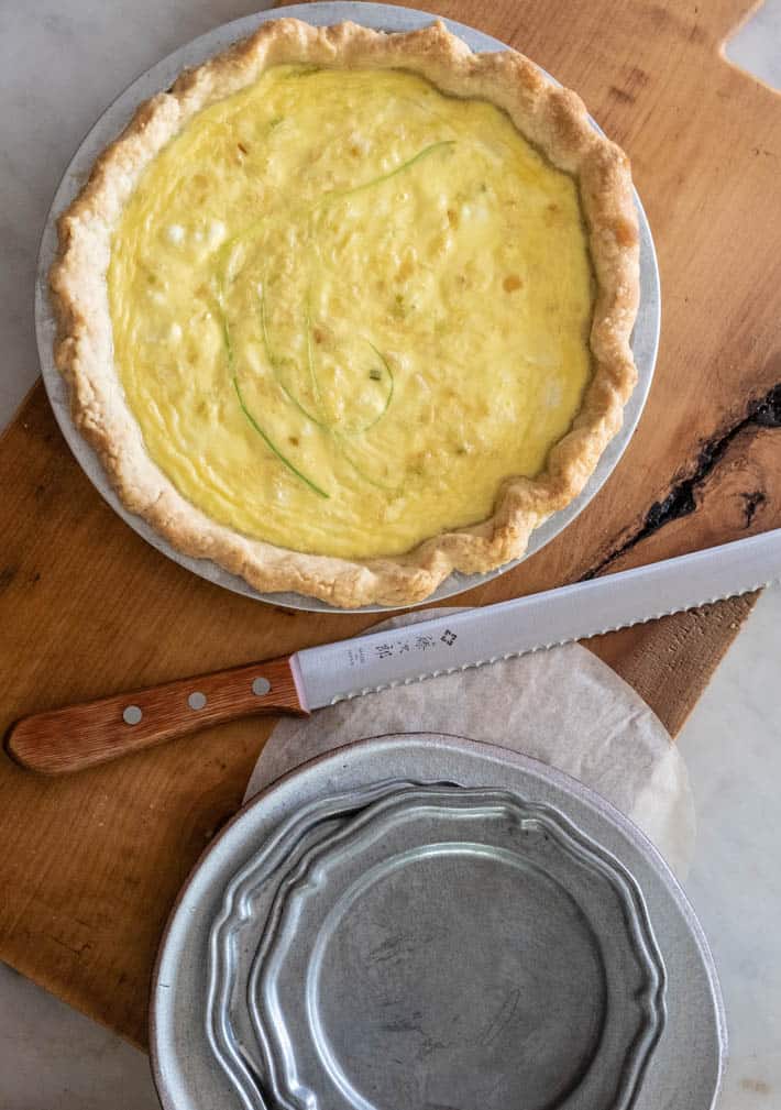 Home made leek quiche set on wood cutting board with vintage pewter plates stacked nearby.