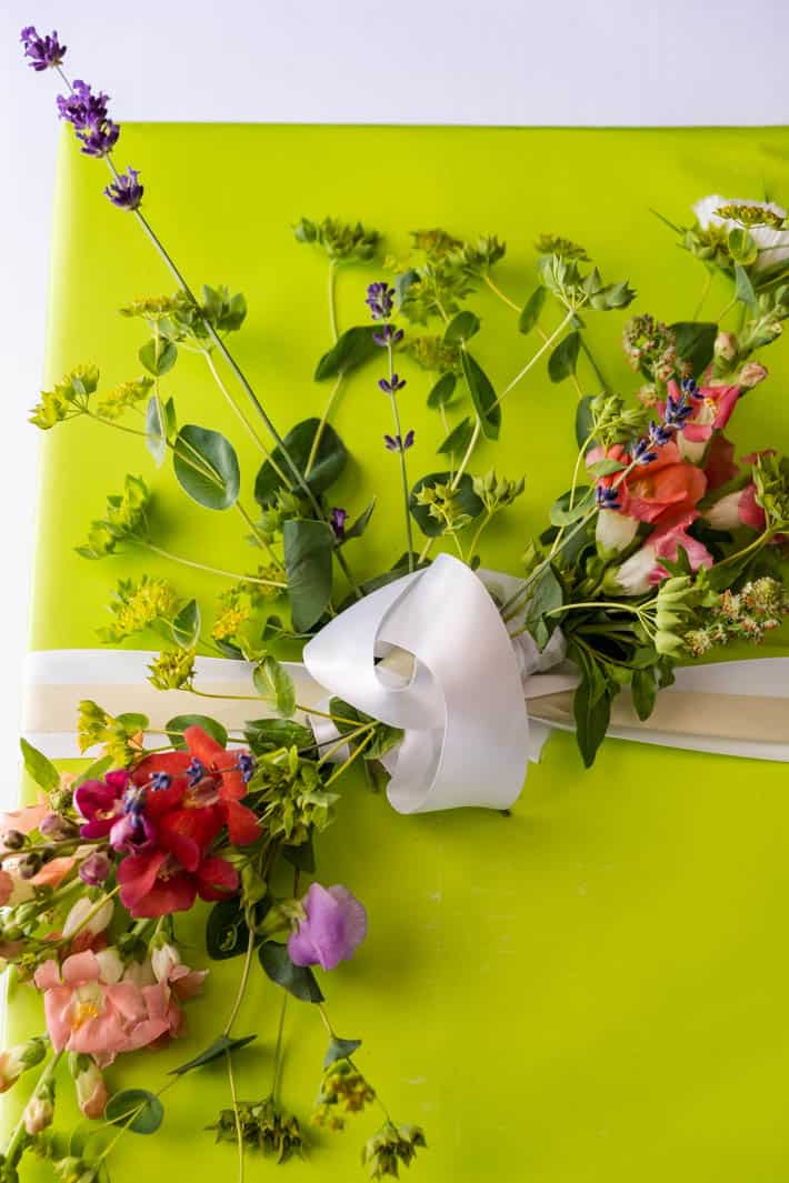 Close-up view of flower bow tied onto gift wrapped in lime-green paper with a white ribbon on white background.