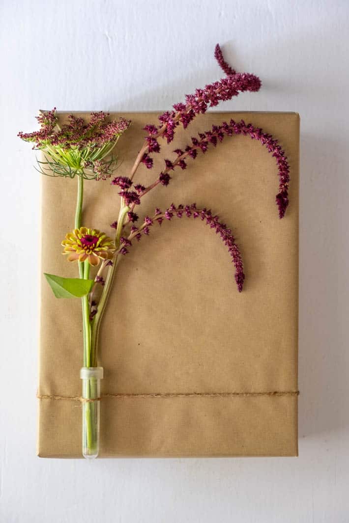 Chocolate Lace Flower, Queen Red Lime Zinnia, Opopeo Amaranth in clear floral vial tied with twine to gift wrapped in brown paper on white background. 