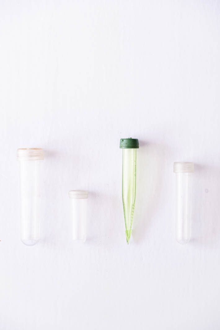 Water vials of various sizes, including three clear and one translucent green vial, on white background. 