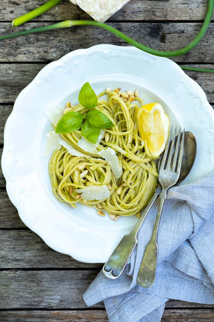 Garlic Scape Pesto on linguine in an antique ironstone bowl, topped with shavings of parmesan, basil leaves and a wedge of lemon.