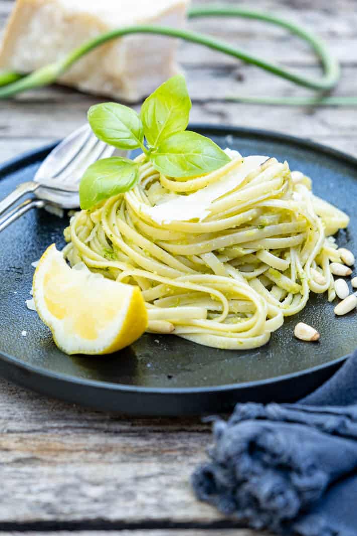 A twirl of linguine dressed with garlic scape pesto on a black plate set on a rough wood table.