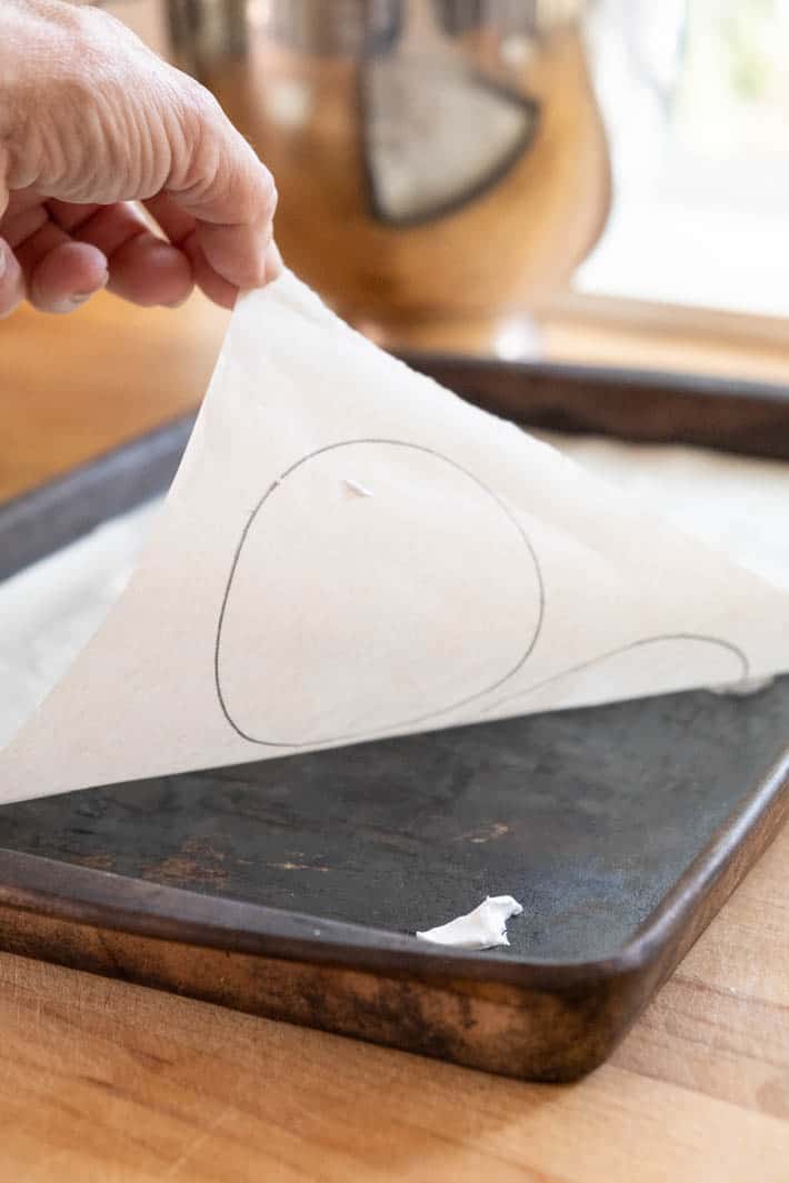 Hand placing parchment paper with circles drawn on it onto a baking tray. 