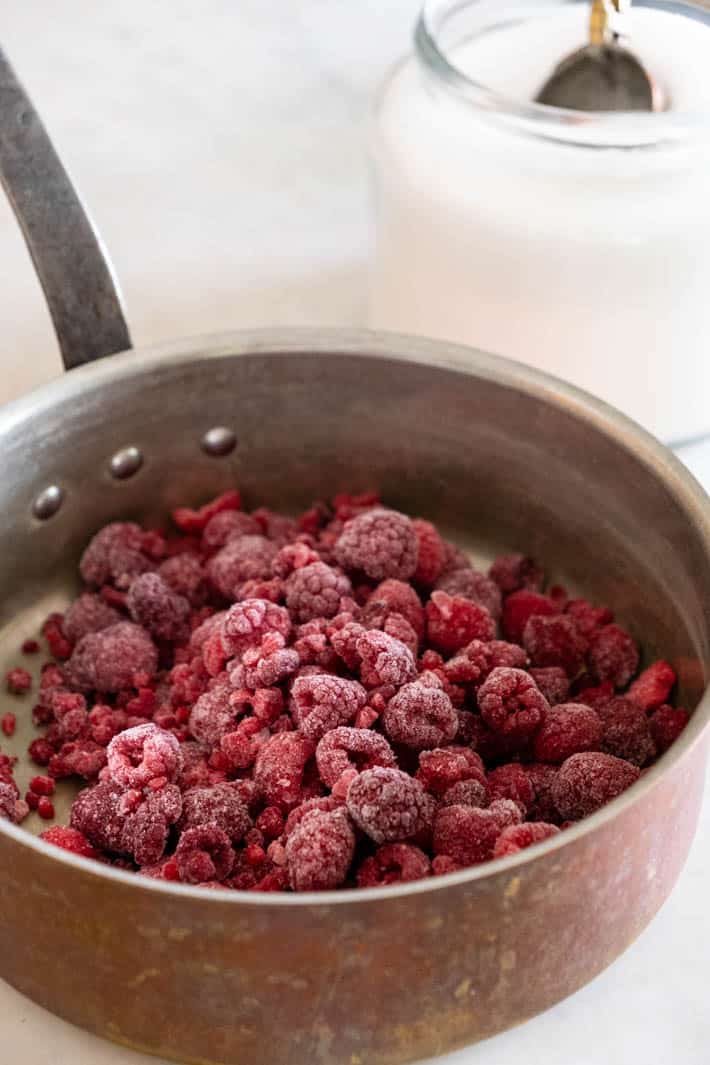 Frozen raspberries in pot with sugar jar in background. 