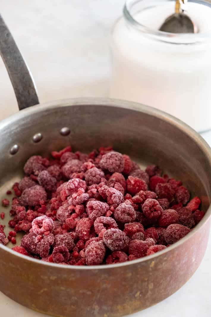 How to make an easy Pavlova with a raspberry compote from The Art of Doing Stuff. Frozen raspberries in pot with sugar jar in background.