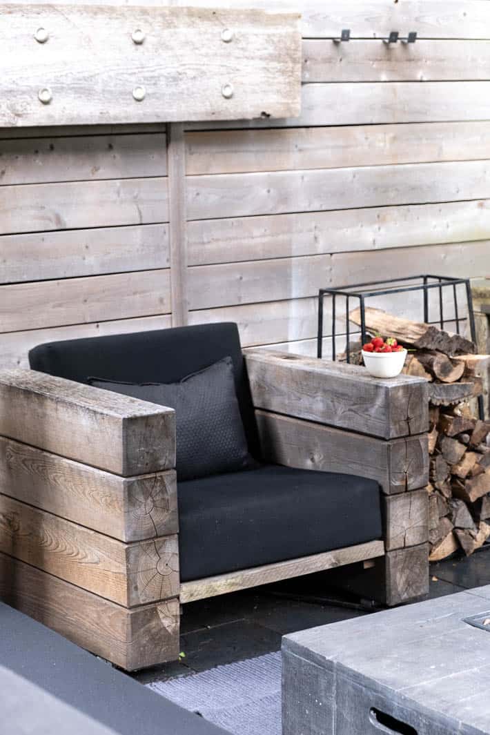 DIY outdoor wooden Restoration Hardware chair with stacked arms in front of horizontal running wood fence.