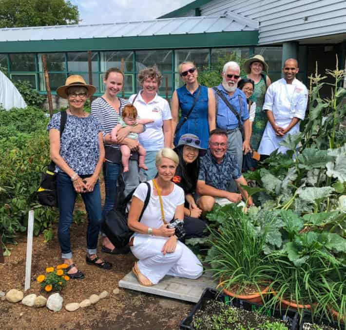 Karen Bertelsen (front, centre) with a group of gardening journalists and enthusiasts posing for a photo in a vegetable garden. A glass building with a green roof can be seen in the background.