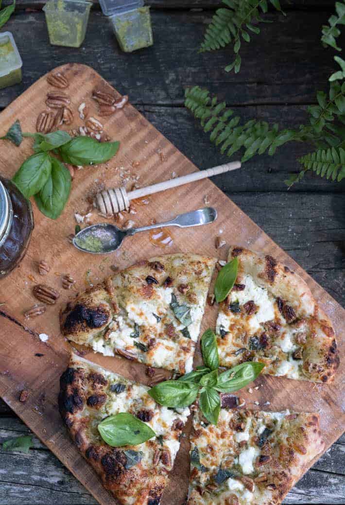 Overhead view of the freshly baked and sliced pesto pizza on a wooden cutting board. 