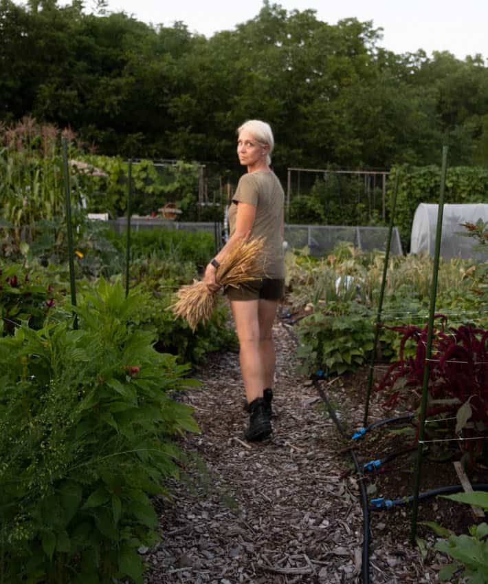 Karen Bertelsen walking away from the camera with her head turned toward the camera in her community vegetable plot. 