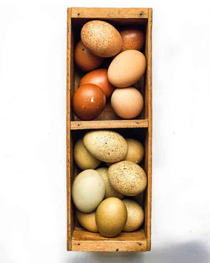 Weird eggs that don't make it into your grocery store carton. Eggs in various shades of brown and pale-olive in a wooden crate on a white background.
