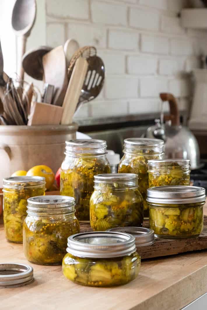 Jars of pickles sitting on Karen Bertelsen's butcher-block kitchen counter top. An ironstone crock with cooking utensils in it and a kettle can be seen in the background. 