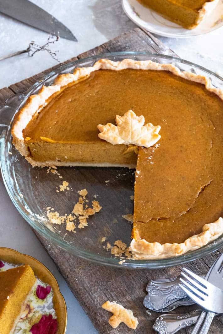 A delicious looking pumpkin pie in a glass pyrex dish with one piece out of it, crumbs around and a