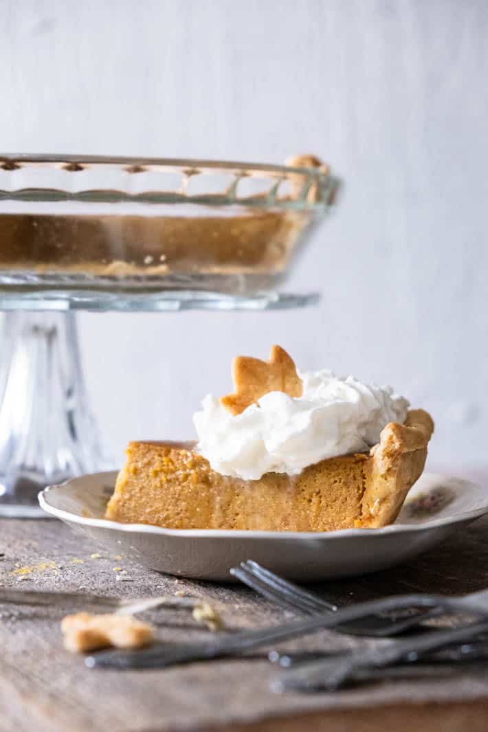 A slice of homemade pumpkin pie topped with whipped cream and a pastry maple leaf.