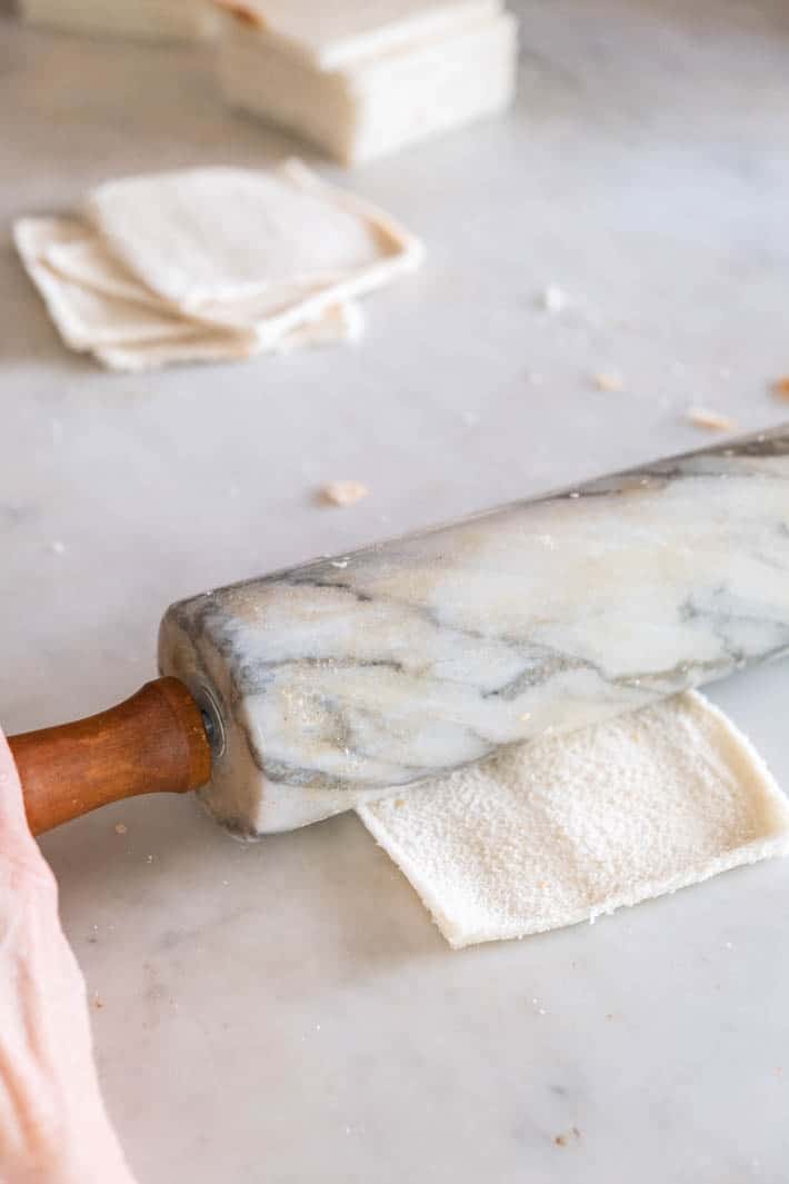 Marble rolling pin being used to flatten white bread, on a marble countertop.