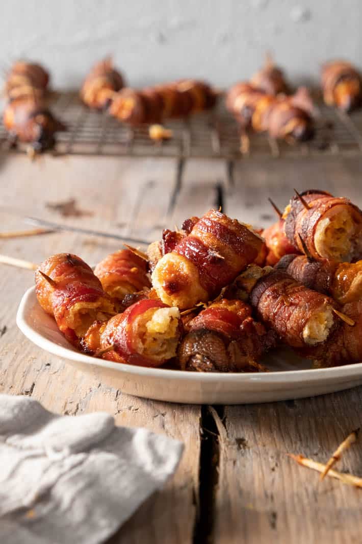 Crispy, salty bacon wrapped around gooey cheese filled bread. THE holiday appetizer. Bacon wraps on ironstone platter.