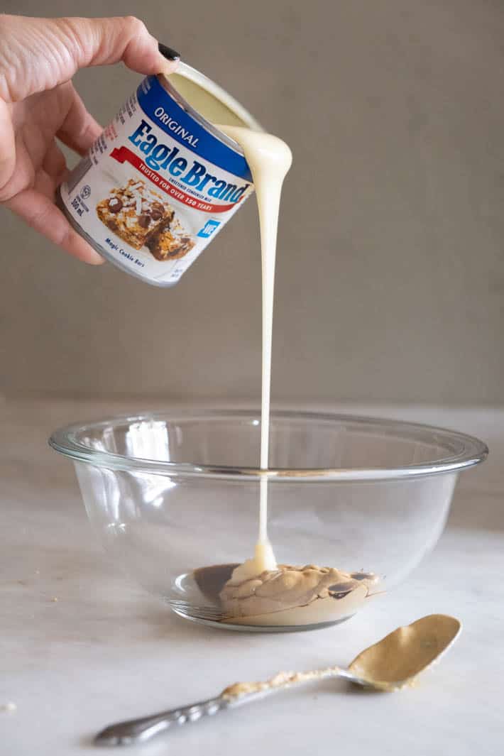 Sweetened condensed milk being poured out of blue and white can into a glass bowl with dijon and Worcestershire sauce.