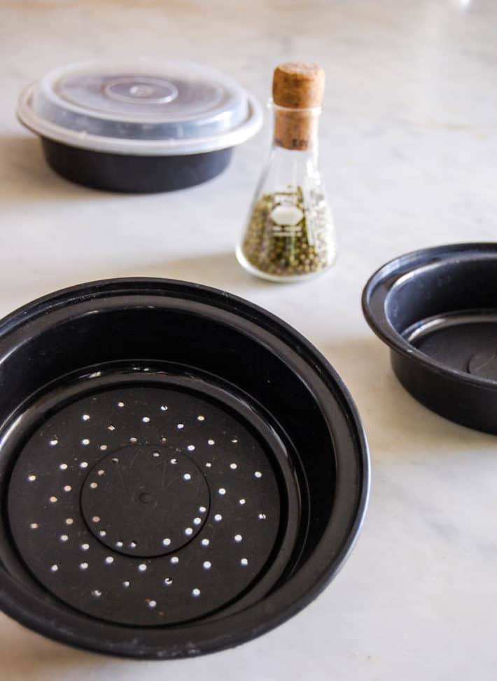 Black plastic takeout container with holes drilled in the bottom being reused for growing mung beans.