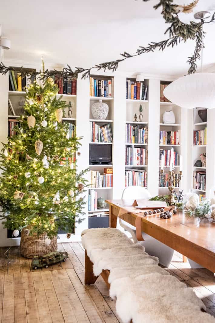 Library dining room combo decorated for Christmas with garland, sheepskins and a live tree in a wicker basket.