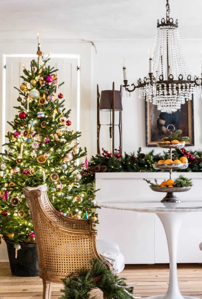 Front room of historic cottage decorated for Christmas with crystal chandelier, tulip table and caned armchair.