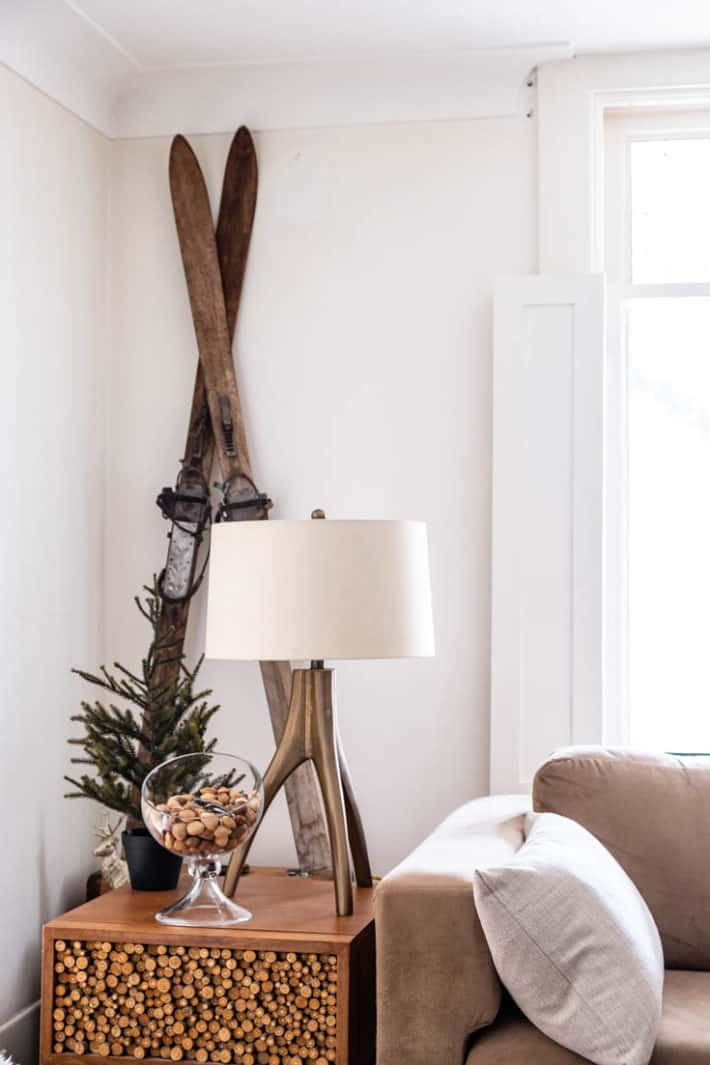 Vintage wood skiis propped against a white wall with an organic brass lamp in front and a modern glass bowl of nuts.