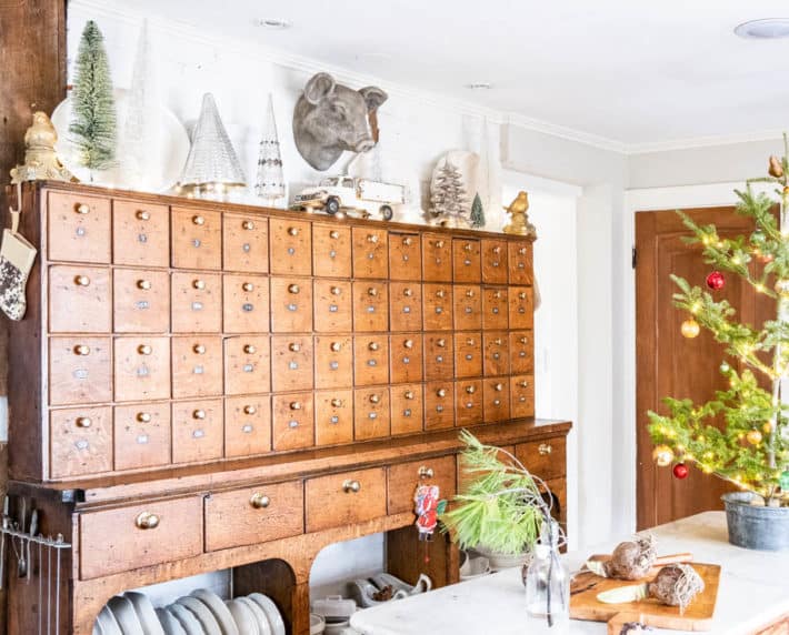 Antique hardware cabinet with Christmas trees on top and ironstone on shelving below.