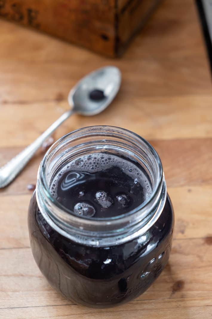 Mason jar on a butcher block counter filled with black beans and cooking liquid to within 1" of the rim.