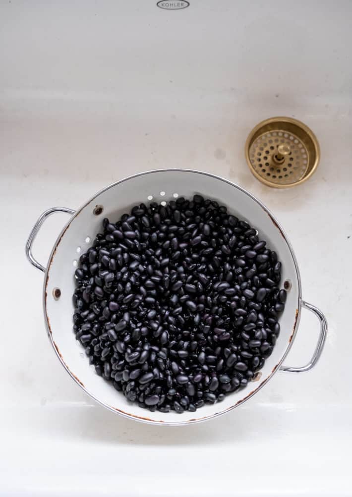 A white enamel colander filled with drained and rinsed black beans.