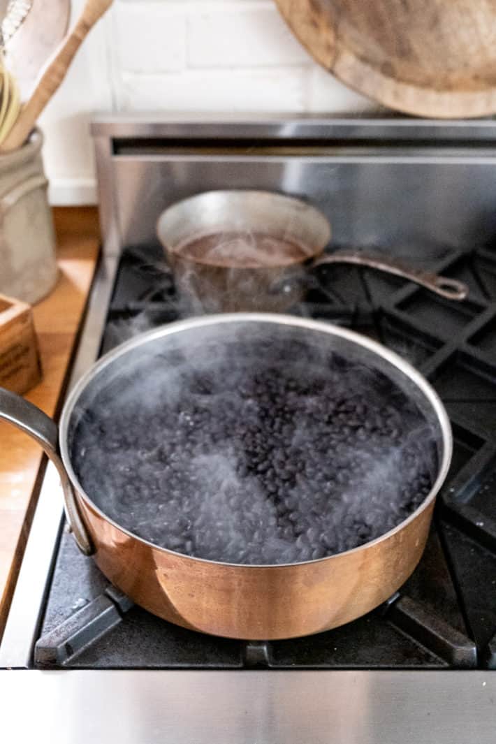 A copper pot filled with black beans simmering to soften them prior to canning.