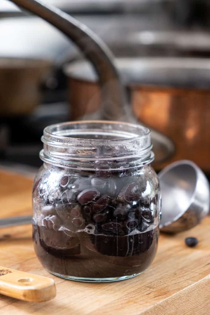 A small mason jar filled with black beans and some cooking liquid ready to be pressure canned.