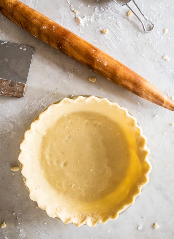 Homemade pie crust unbaked in a pyrex dish on a marble countertop dusted with flour.