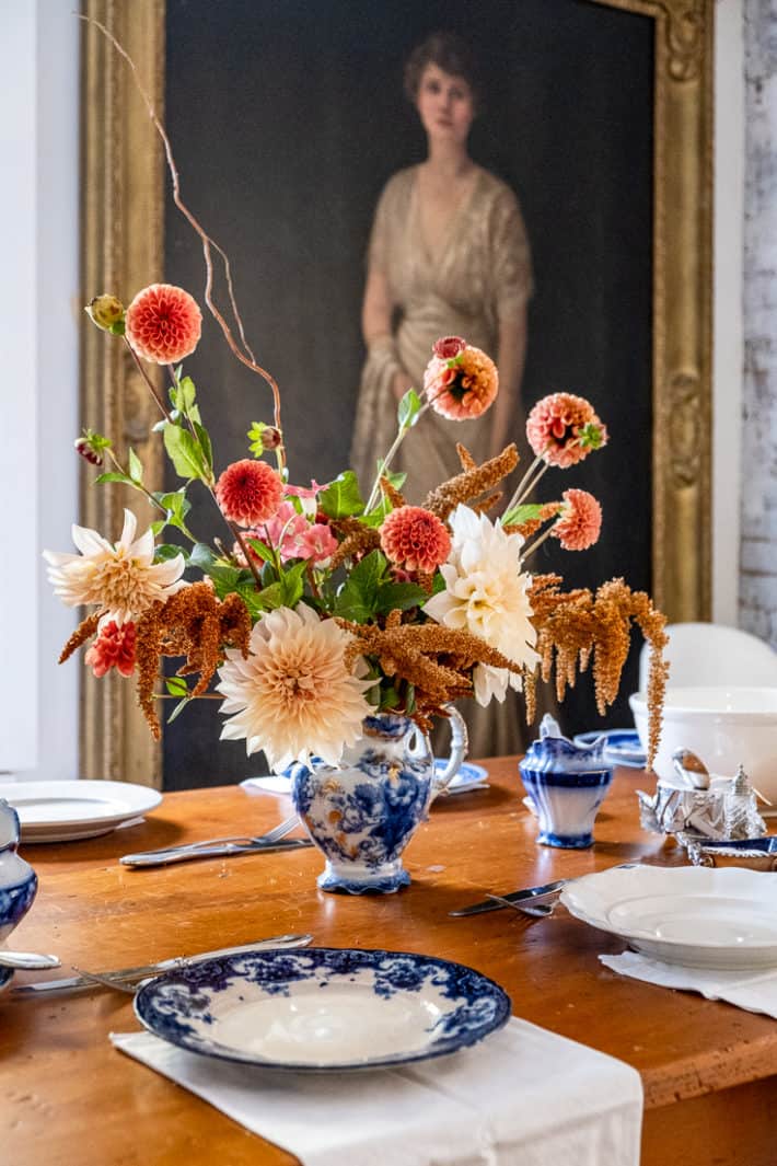 A Thanksgiving centrepiece of ice cube dahlias, hot biscuits amaranth and cornel bronze dahlias sits in a flow blue jug.
