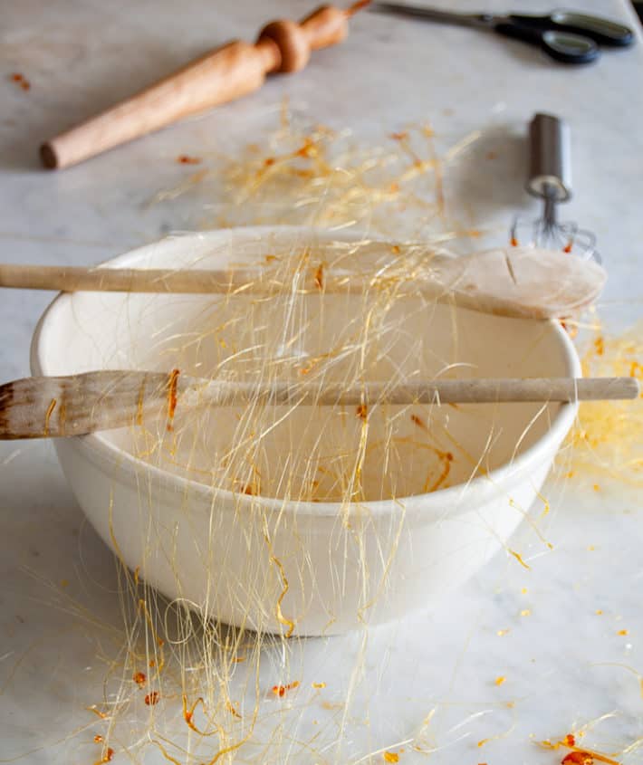 Strands of gold spun sugar flung across 2 wood spoons over a bowl to create threads.