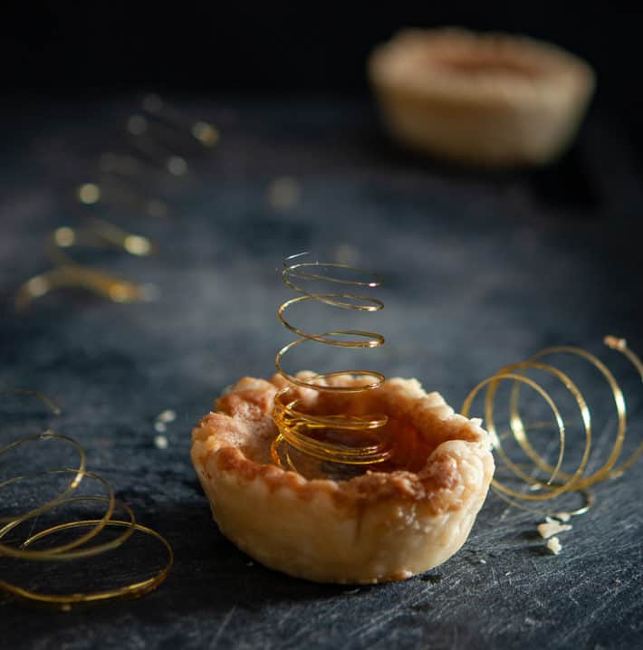 A gold coil spring of sugar coming out of the centre of a butter tart.