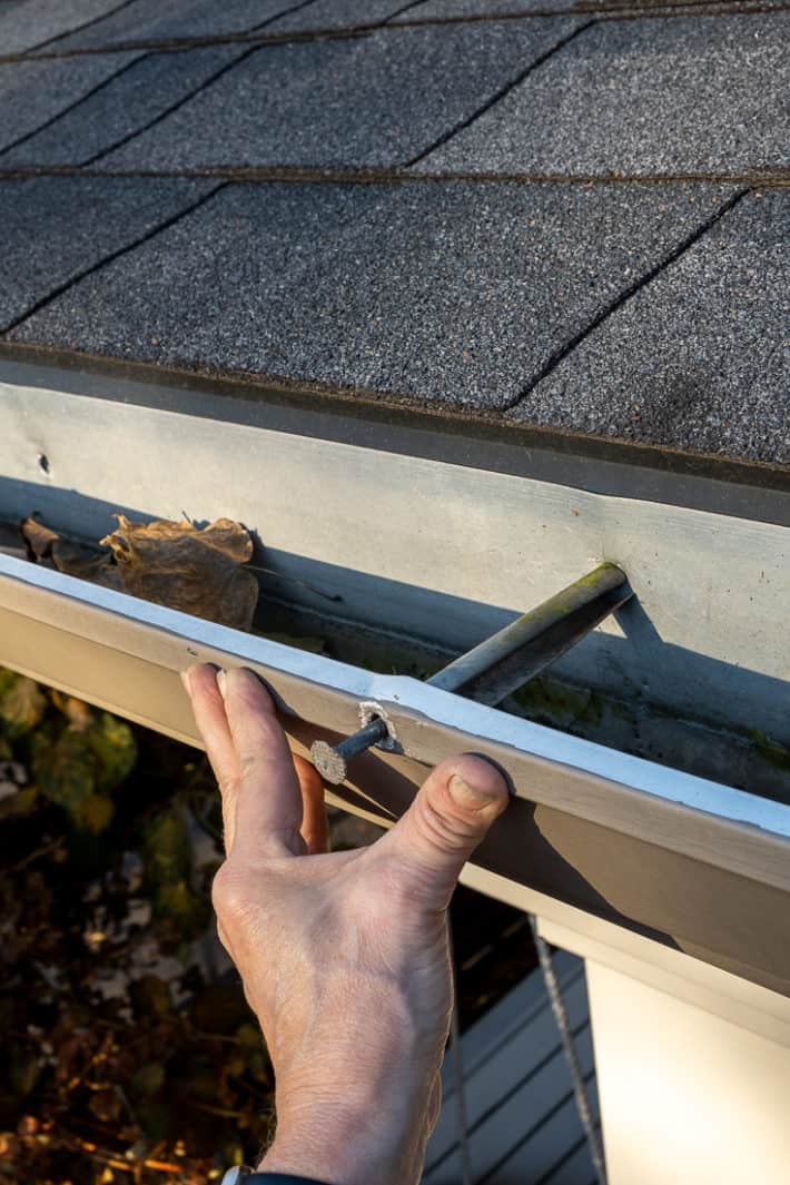 A hand pushing a loose gutter tight against the fascia.