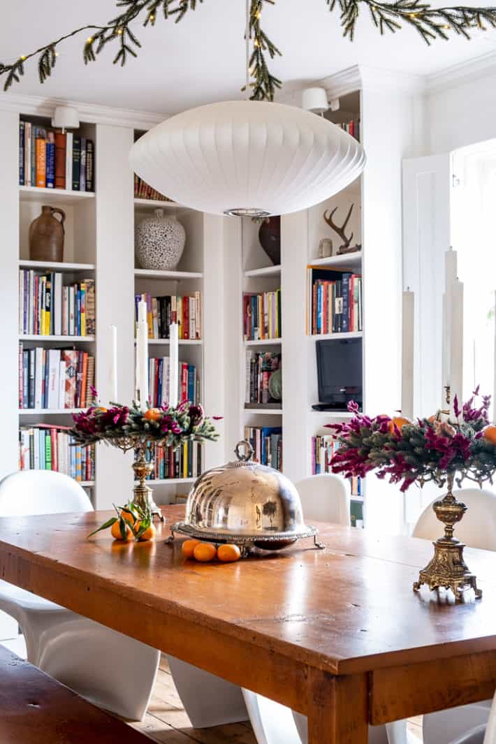 White bookcases surround a wood harvest table decorated with candelabras festooned with dried flowers.