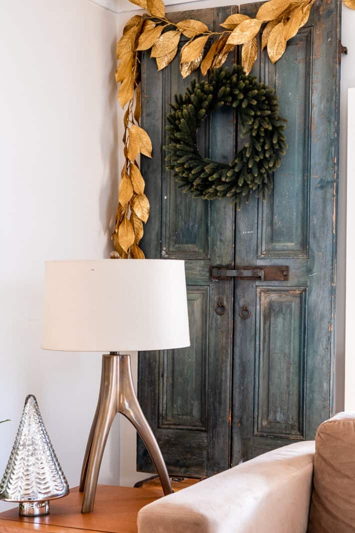 Antique blue painted French shutters with iron hardware decorated with a plain Christmas wreath and gold leaf garland.