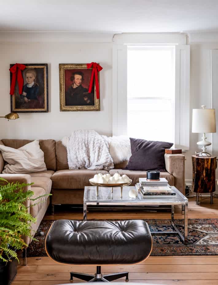 A cozy living room with antique wood floors and dark, portraits on the white walls, accessorized with red velvet fabric bows.