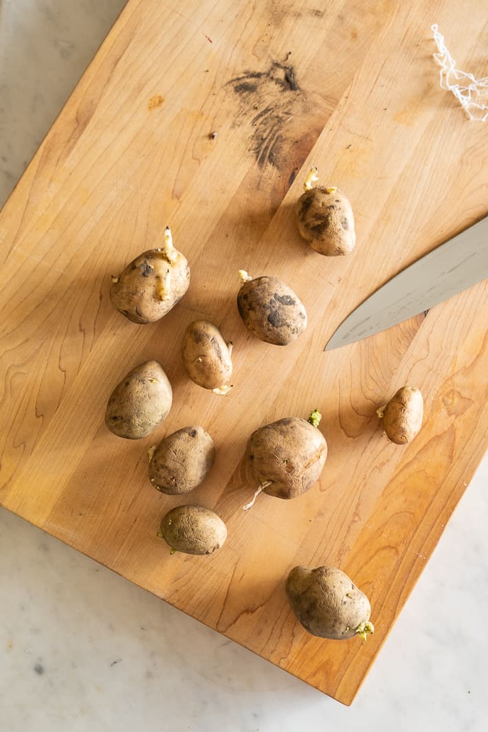 Seed potatoes lay on a cutting board seen from overhead.